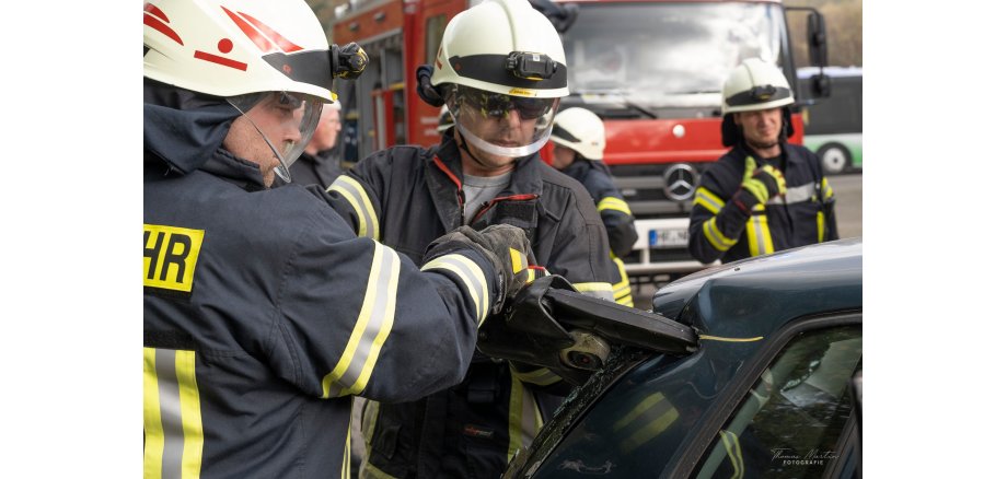 Zwei Feuerwehrmänner schneiden mit hydraulischem Rettungsgerät ein Auto auf